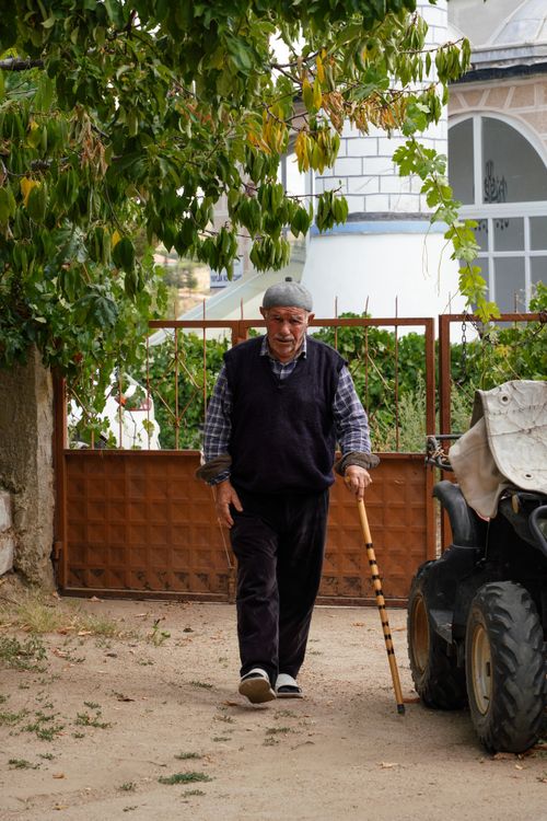 Free Senior man walking with a wooden cane near a rural home. Calm and peaceful setting. Stock Photo