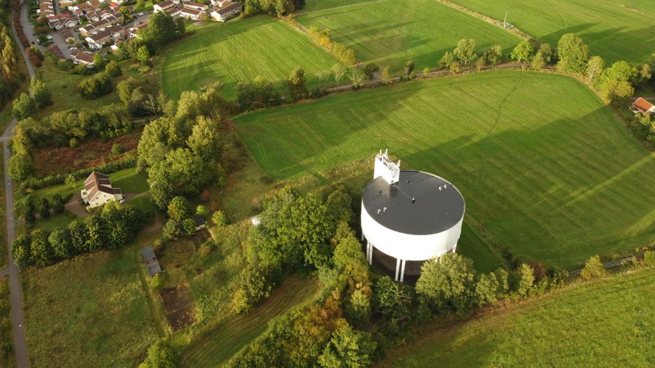 Aerial view of a water tower surrounded by green fields and residential areas in a serene landscape.
