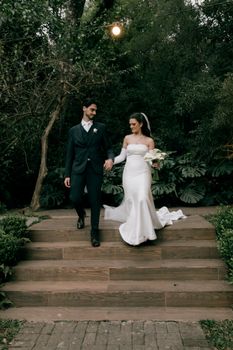 Bride and groom walking down garden steps in a serene outdoor setting, showcasing elegance and style.