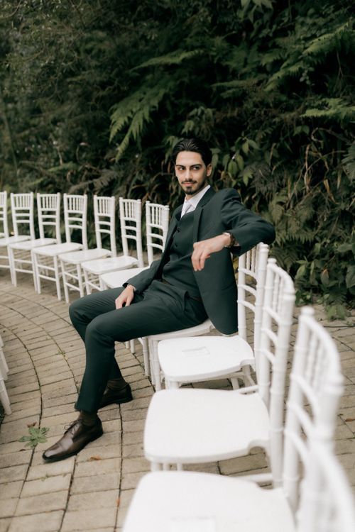 Free A man in a suit sits confidently among white chairs in an outdoor setting. Stock Photo