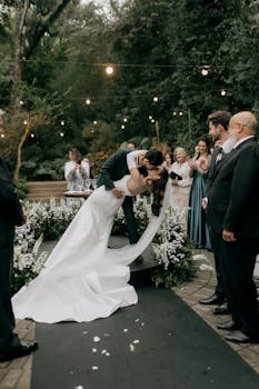 A couple's romantic kiss at an outdoor wedding ceremony surrounded by guests and flowers.