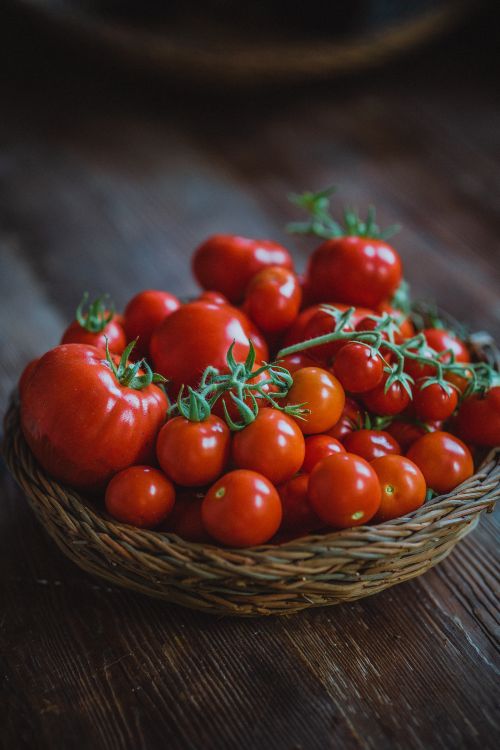 Free Vibrant fresh tomatoes in a wicker basket on a rustic wooden table, perfect for culinary and natural food themes. Stock Photo