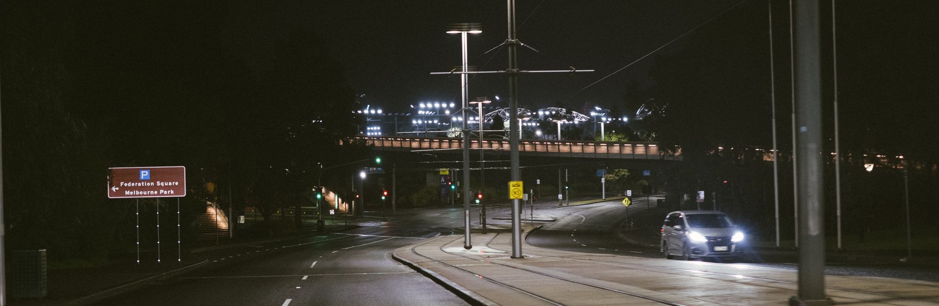 Night view of a road in Melbourne, featuring car headlights and city lights.