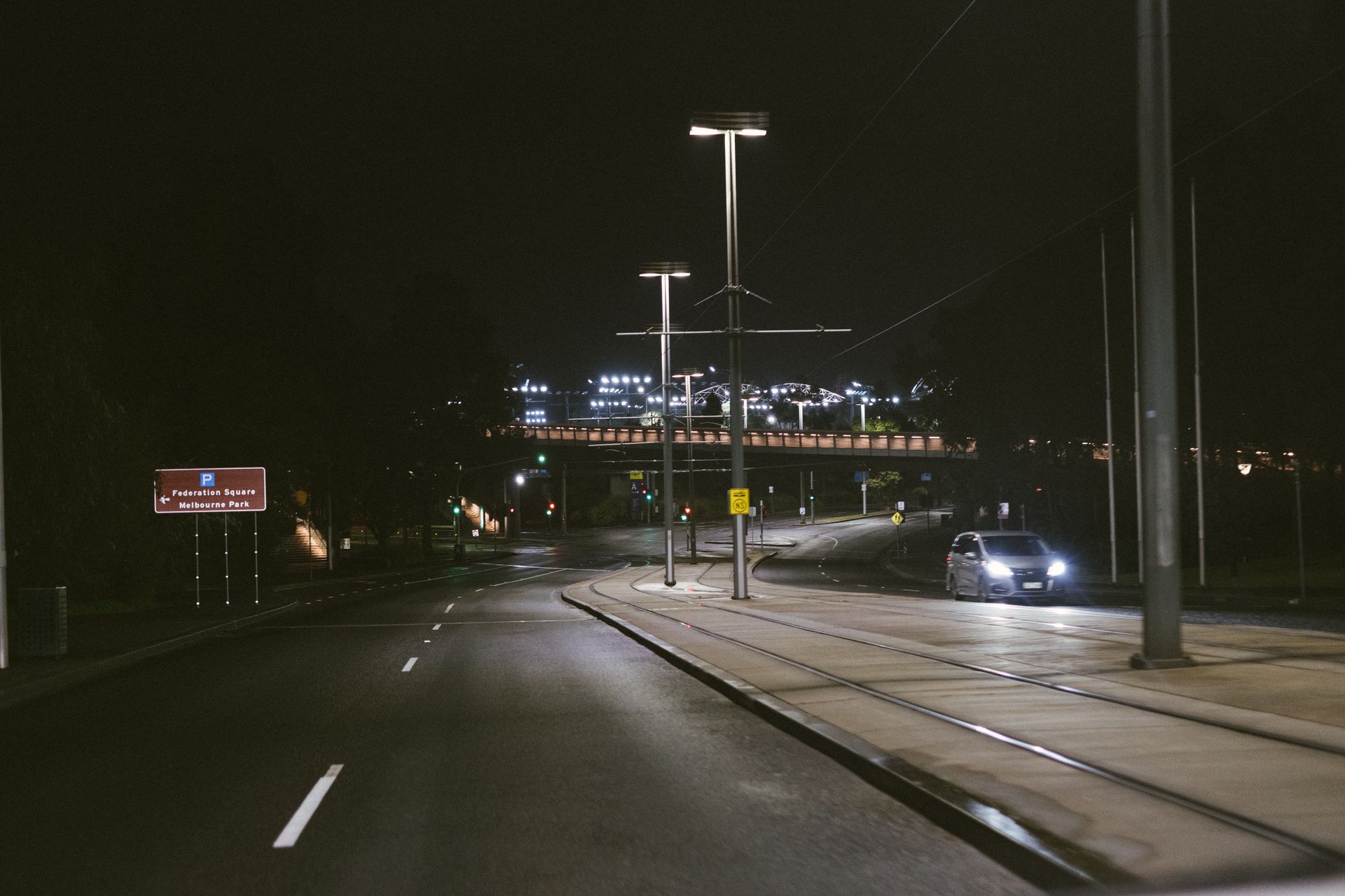 Night view of a road in Melbourne, featuring car headlights and city lights.