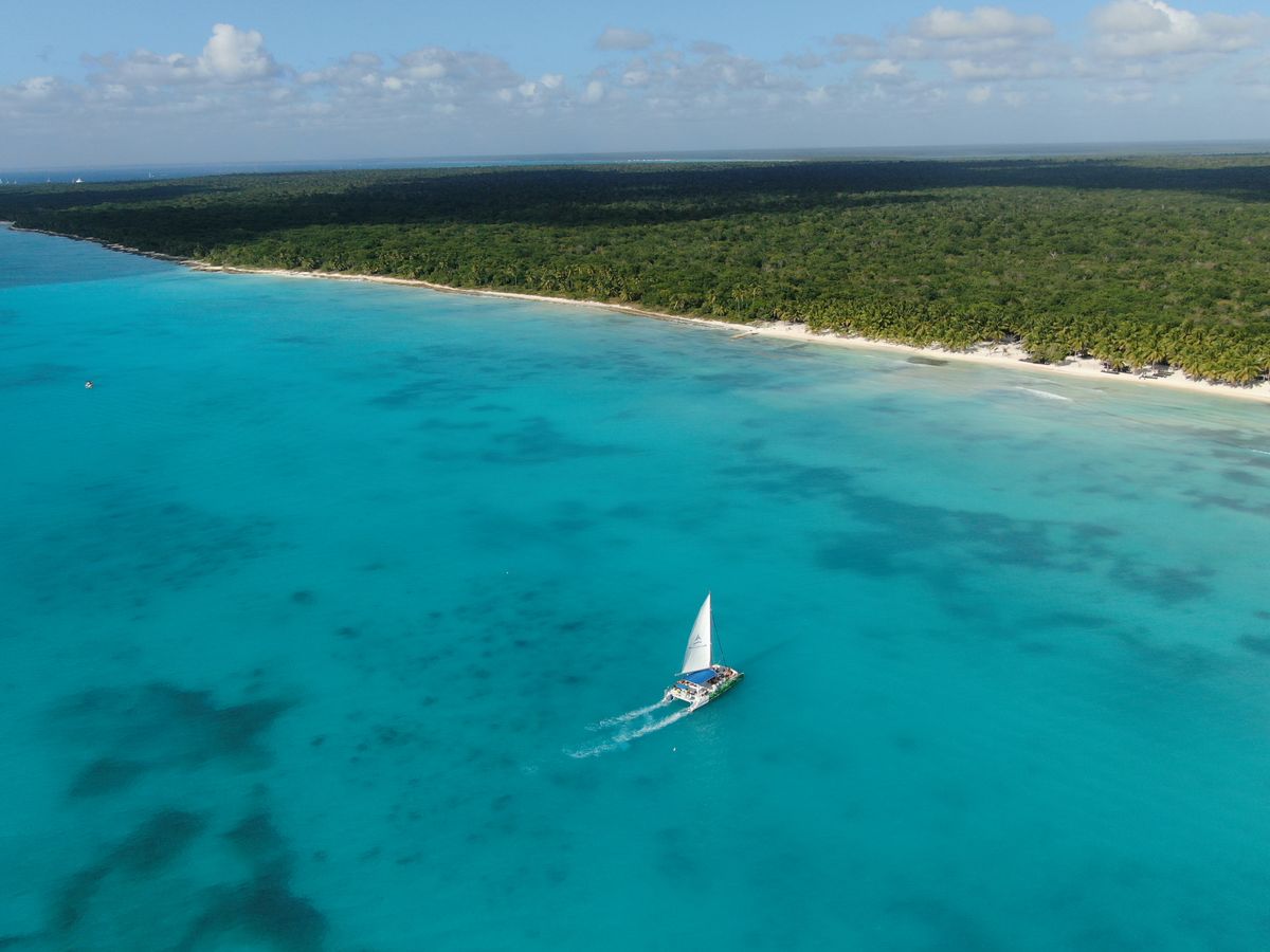 Un velero se desliza a lo largo de una costa turquesa prístina bajo un cielo soleado.
