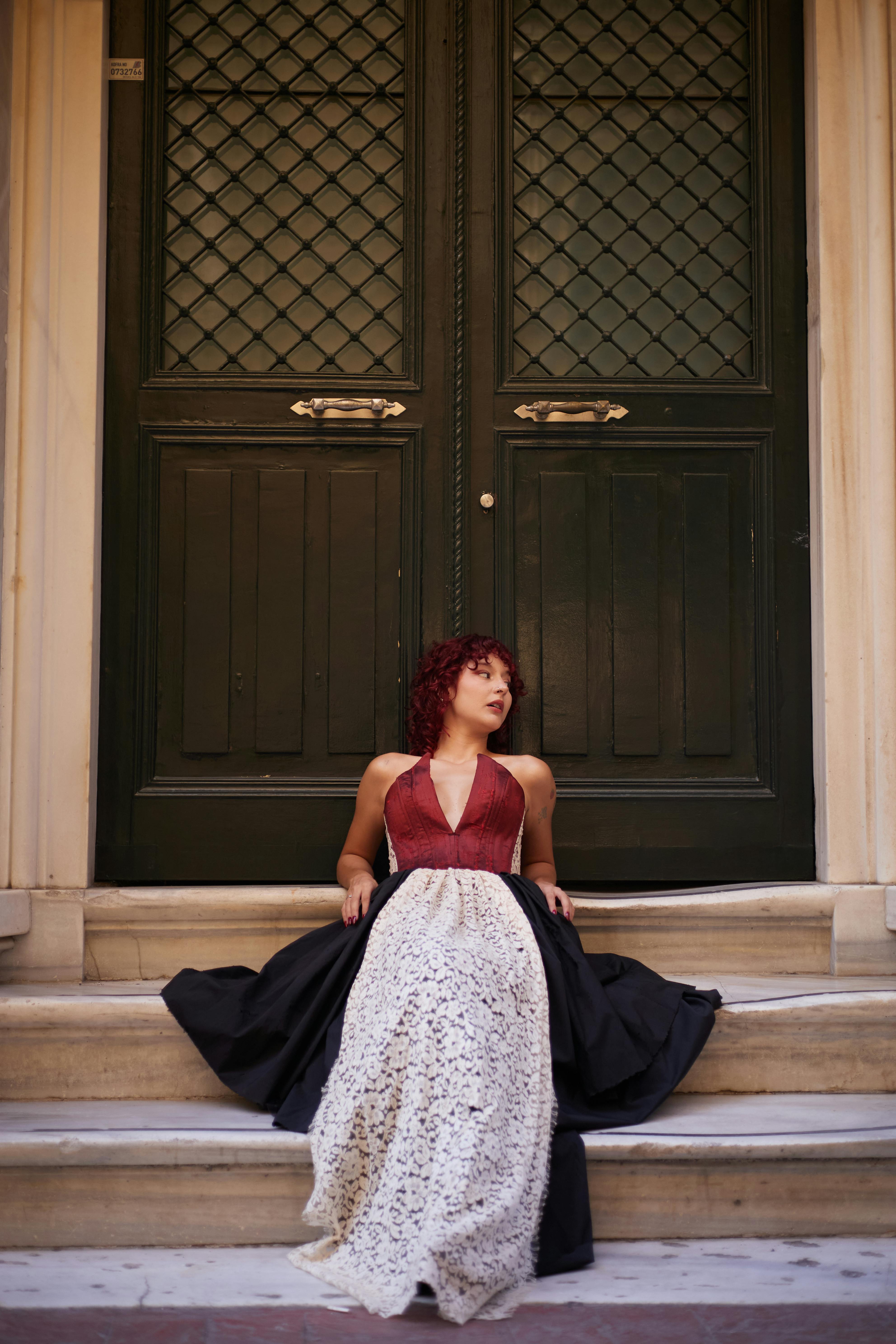 An elegant woman in a formal evening dress sits on steps by a historical door in Istanbul.