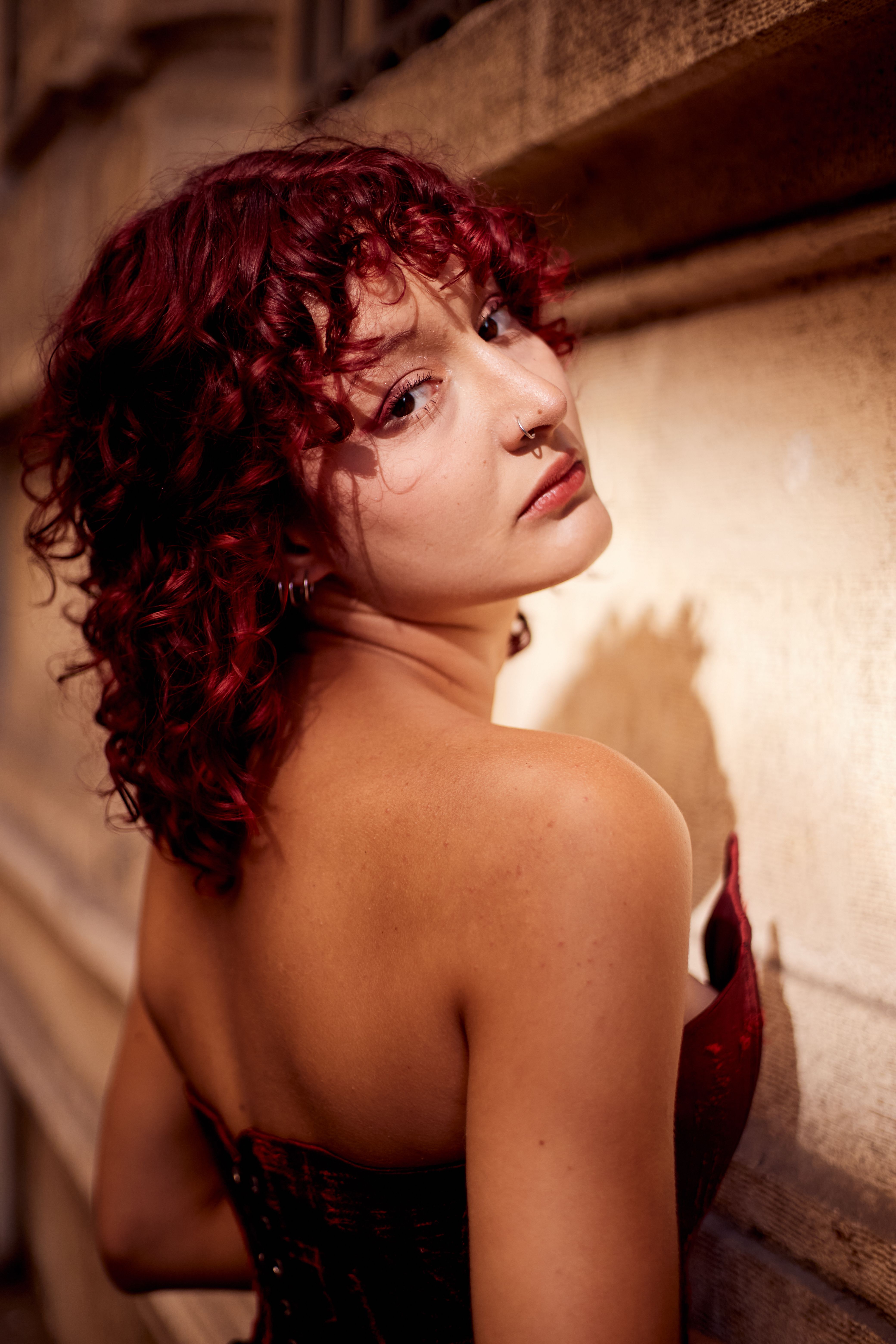 Stylish woman with red hair and tattoos posing against a textured wall in İstanbul.