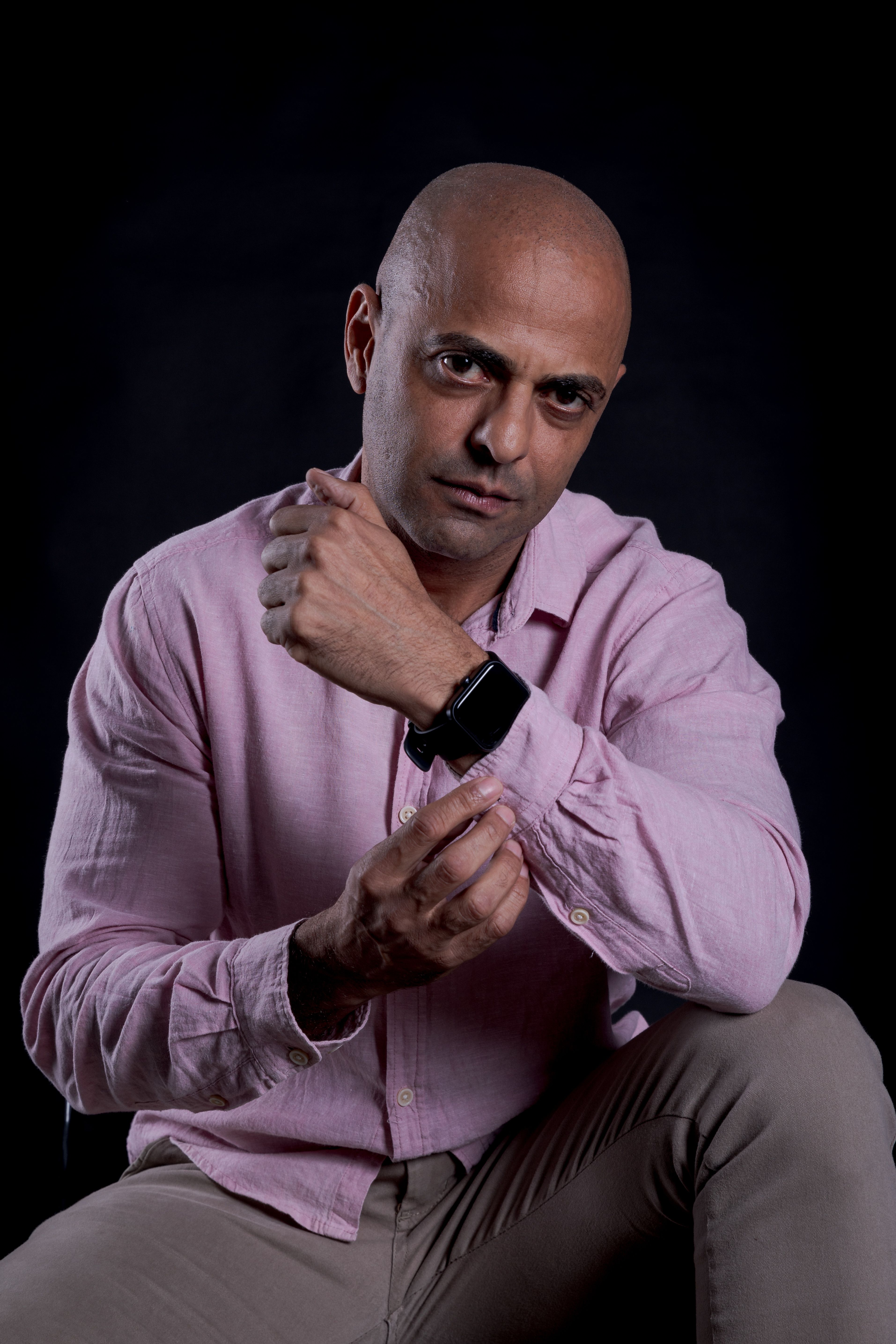 De franc Retrat d'un home calb i segur de si mateix, amb una camisa rosa i un rellotge intel·ligent, assegut sobre un fons fosc. Foto d'estoc