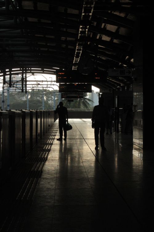 Free Silhouetted commuters at a dimly lit urban train station during dusk, creating a moody atmosphere. Stock Photo