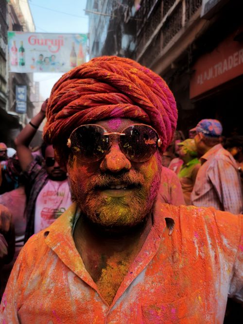 Free Man covered in colorful powders during Holi festival in bustling street. Stock Photo