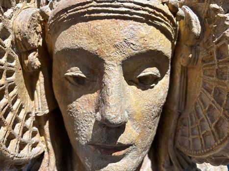 Detailed close-up of an ancient, intricately carved stone statue in sunlight.