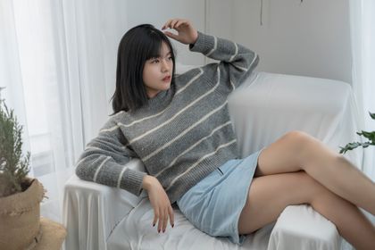 Relaxed woman in cozy sweater lounging on couch with natural light — photo by Đan Thy Nguyễn Mai on Pexels