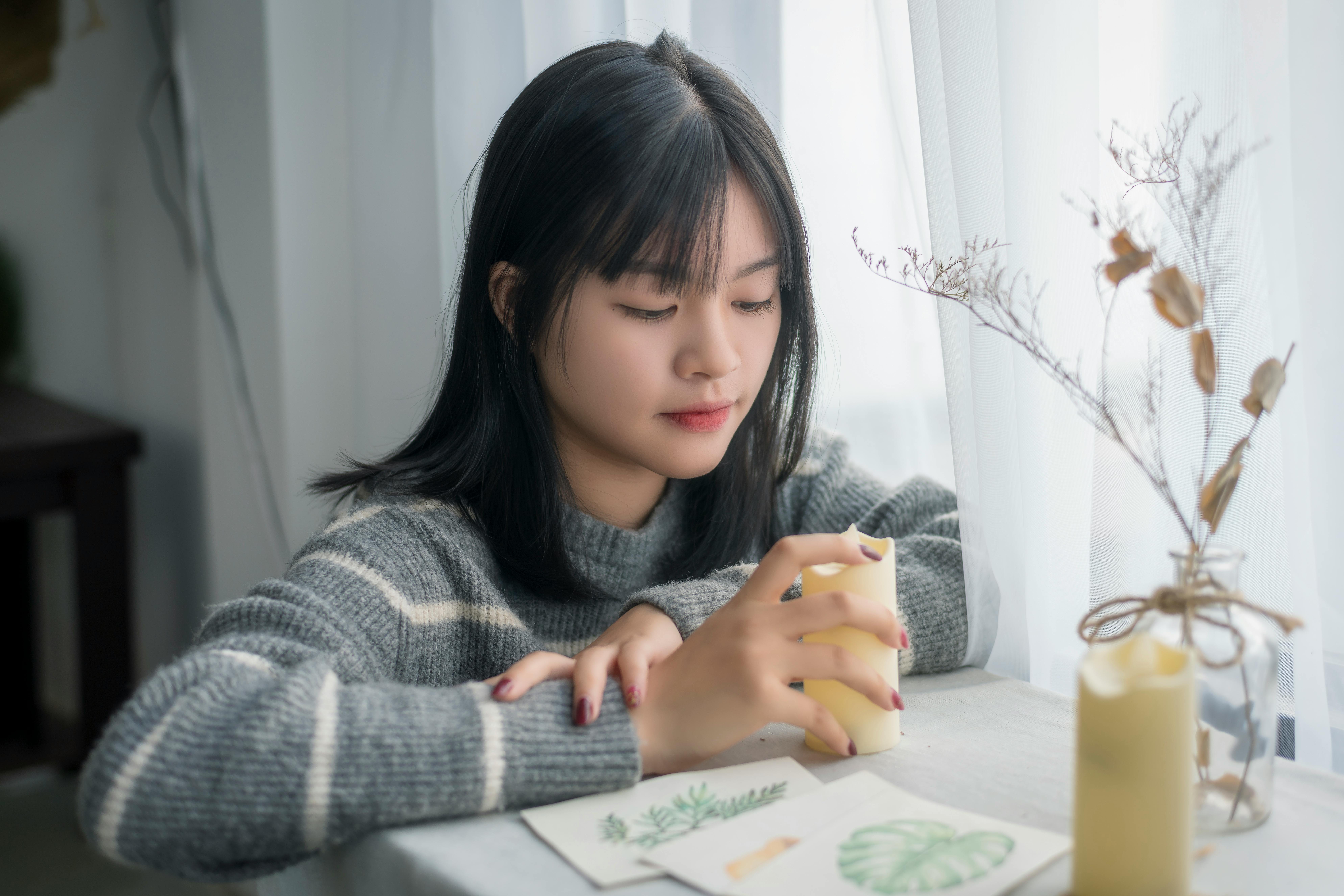 A young woman sits thoughtfully holding a candle in a cozy indoor setting.