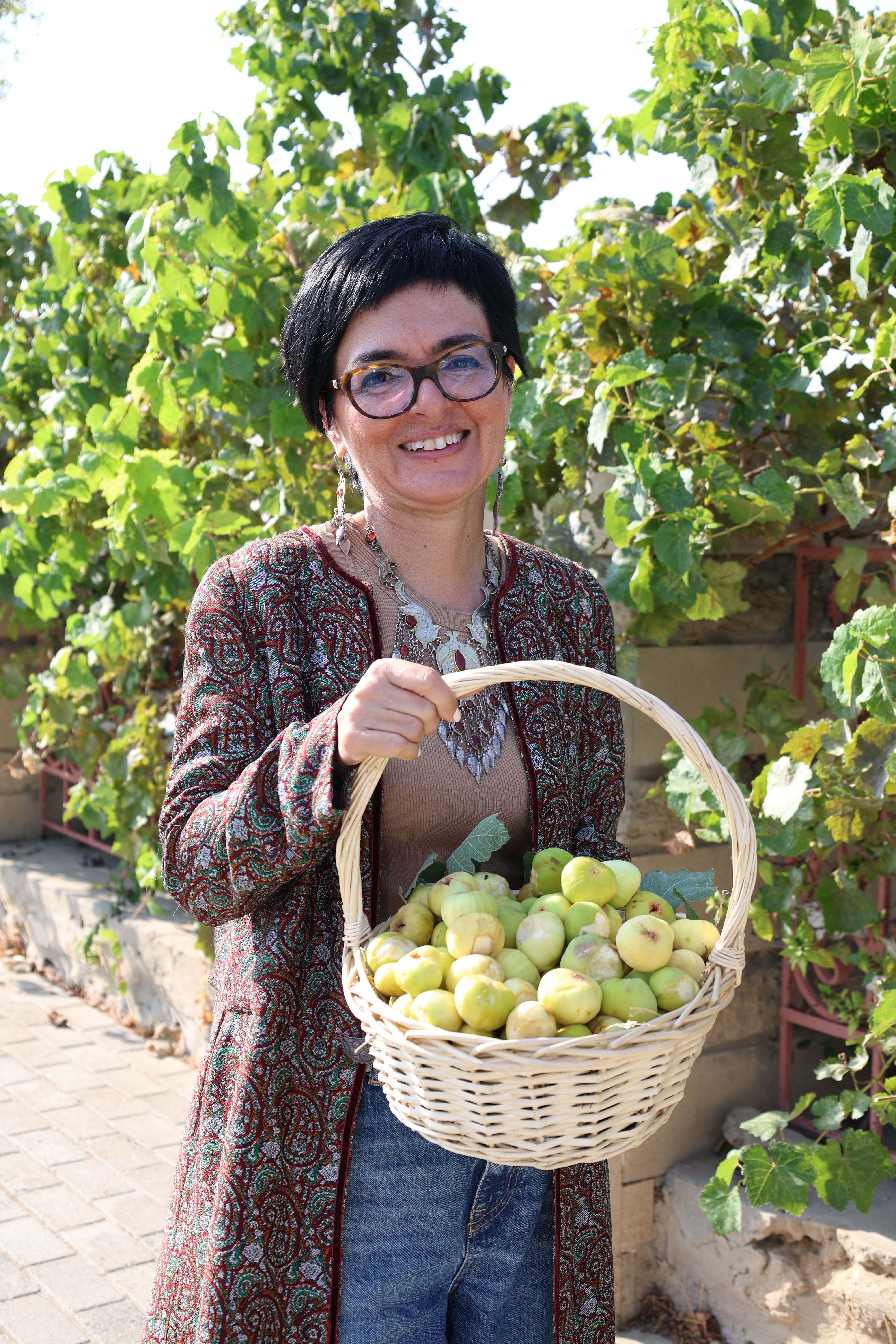 Smiling woman holding a basket of apples in a sunny garden, enjoying a bountiful harvest.