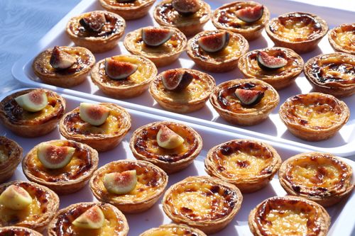 Free A delightful display of fresh fig and custard tarts arranged neatly on trays under bright daylight. Stock Photo