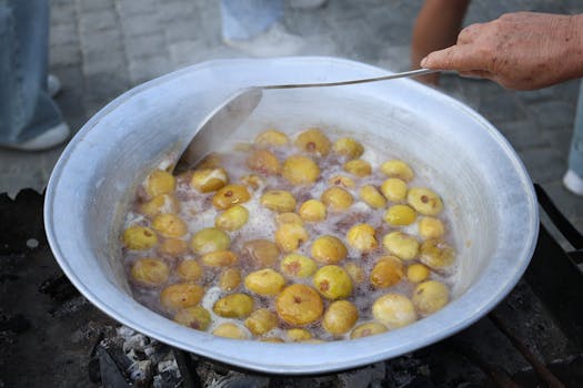 Large outdoor pot boiling yellow plums. Traditional cooking process with hand stirring.