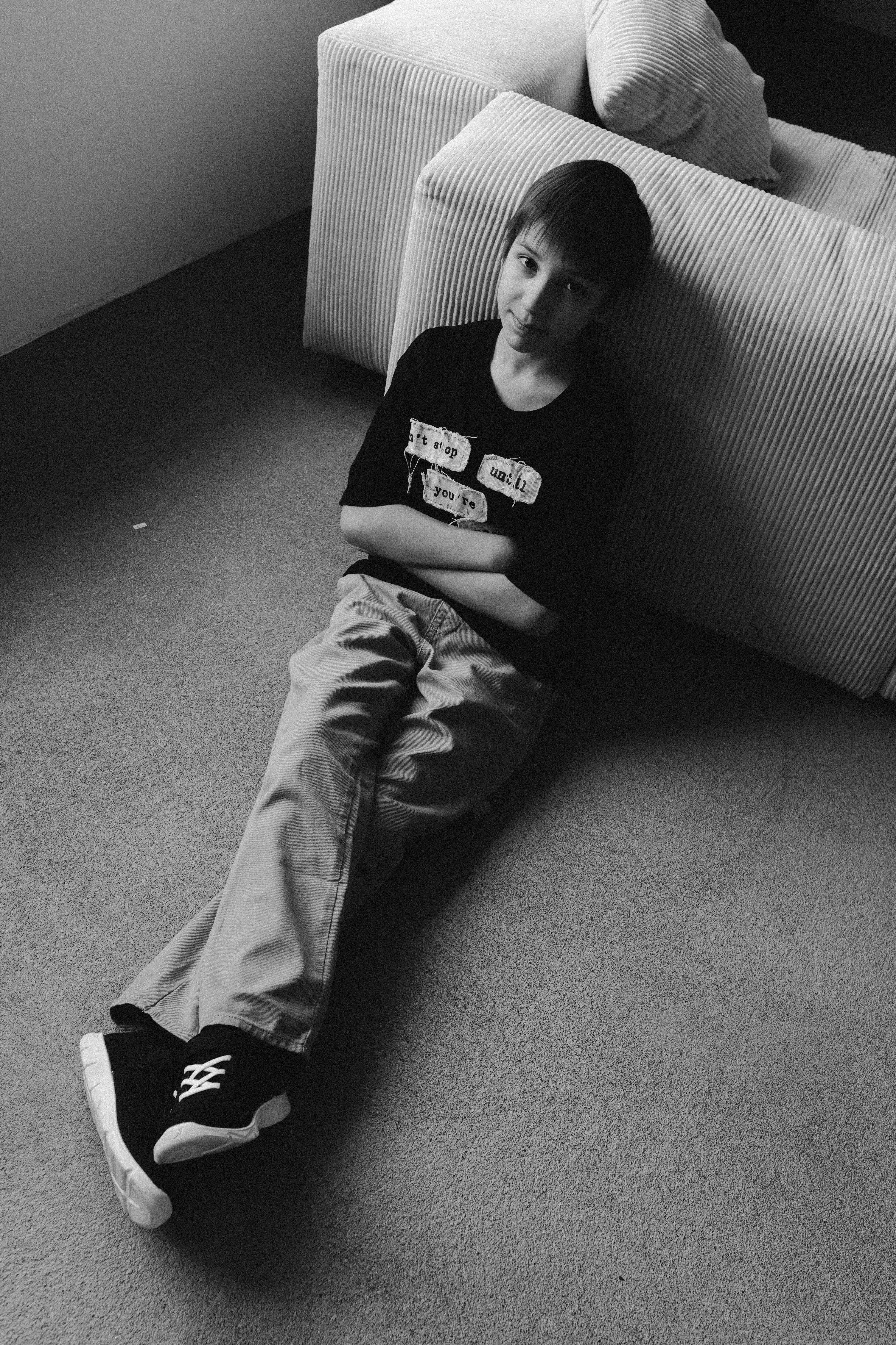 Black and white image of a boy seated on the floor indoors, looking pensive.