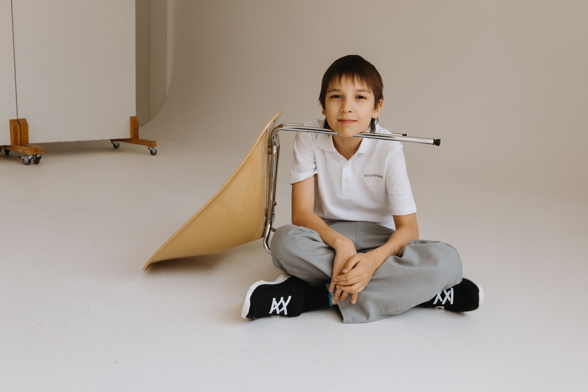 A young boy sits on the studio floor next to an overturned chair, smiling warmly.