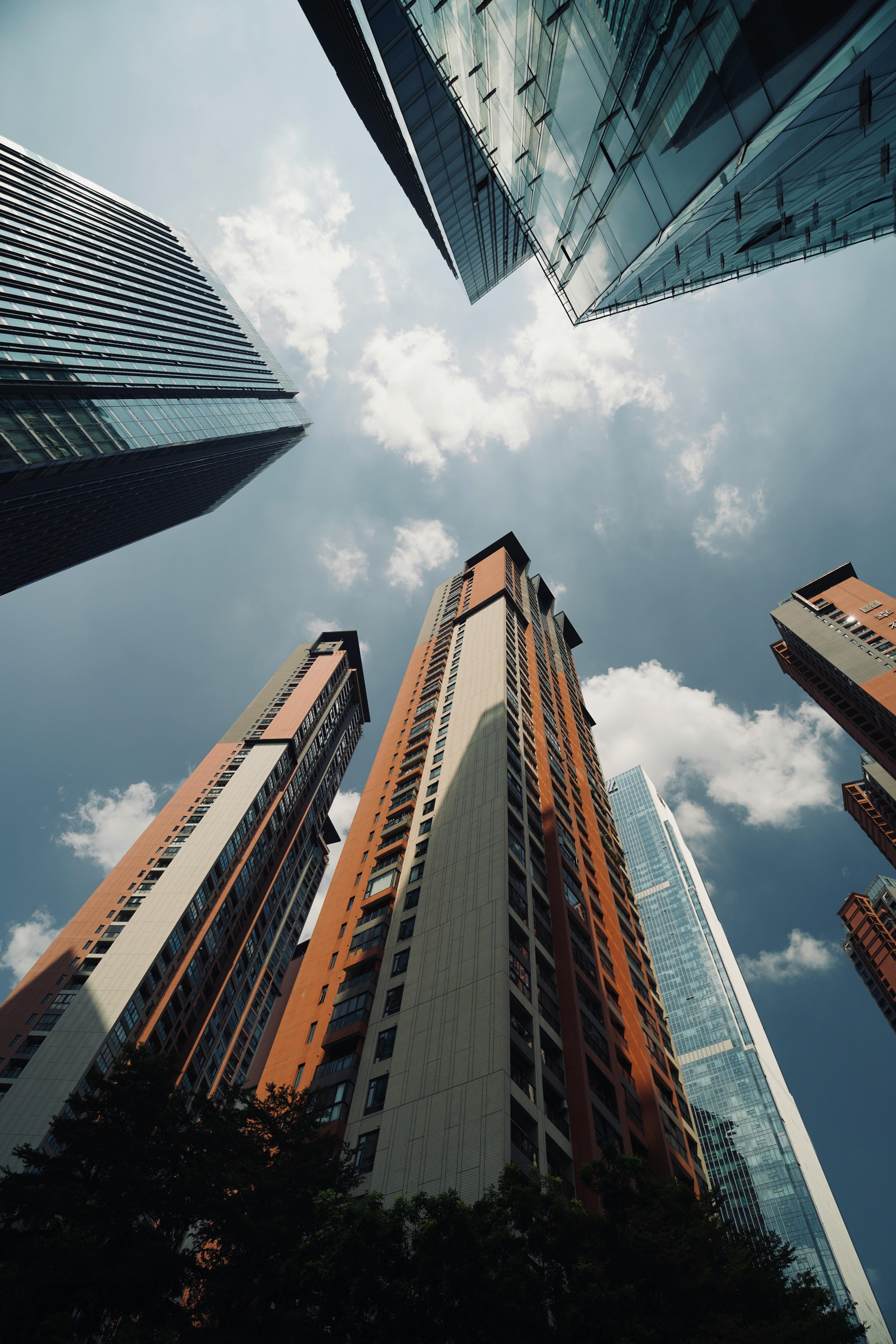 Upward view of modern skyscrapers with blue sky and clouds, creating a dramatic cityscape.