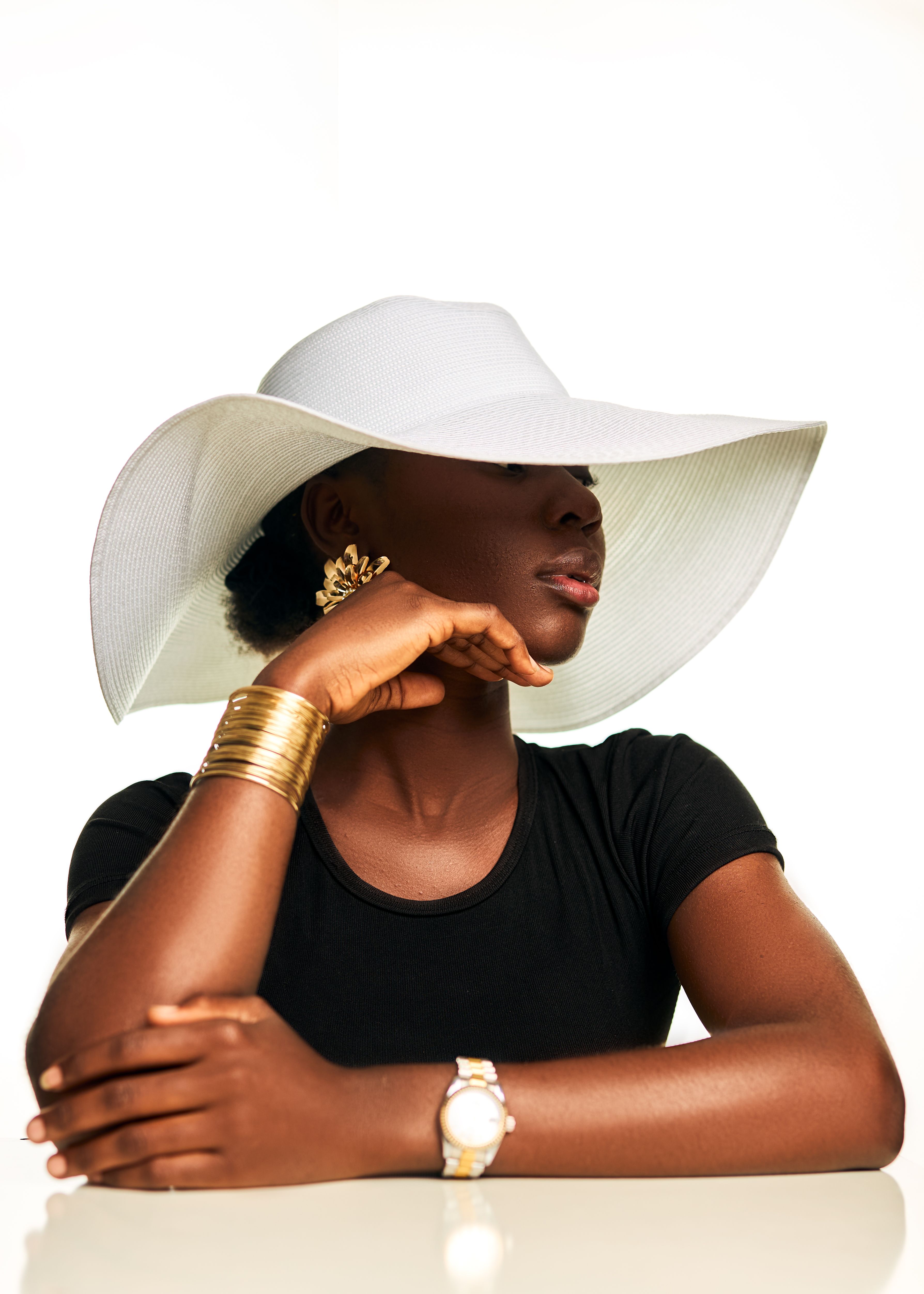 Portrait of a woman wearing a wide-brimmed hat and elegant jewelry against a white background.