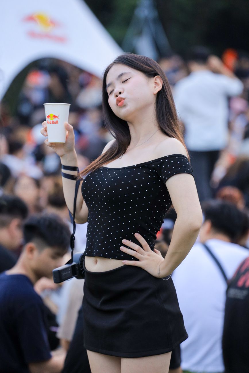 Young woman posing with a drink in Hanoi's vibrant outdoor festival setting.