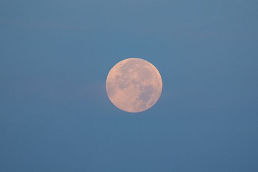 Captivating full moon against a serene blue sky during twilight, showcasing lunar details.
