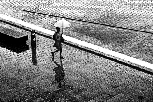 A black and white image captures a woman walking with an umbrella on wet cobbled streets in Istanbul.