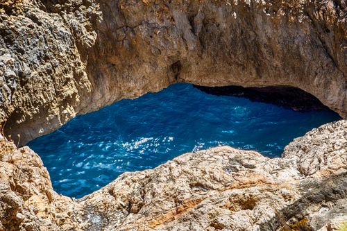 Free Stunning natural rock arch with vibrant blue ocean below, captured in bright sunlight. Stock Photo