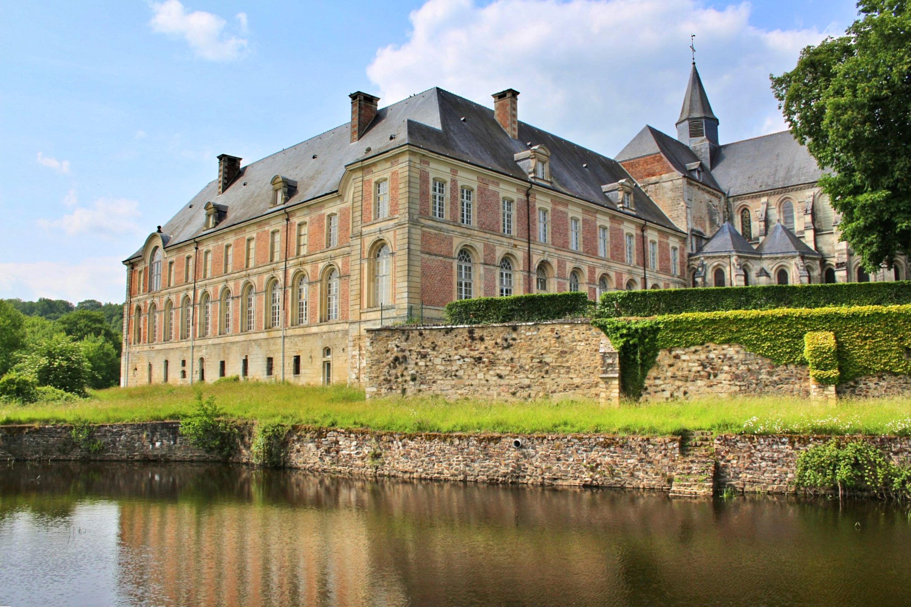 A picturesque view of a historic abbey surrounded by lush greenery and a tranquil pond.