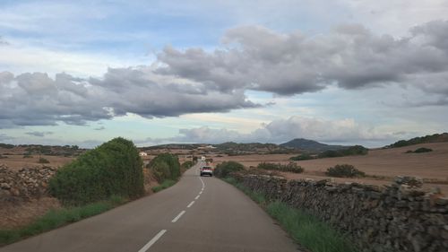 Free A car travels down a scenic rural road surrounded by open countryside and dramatic cloud-filled skies. Stock Photo
