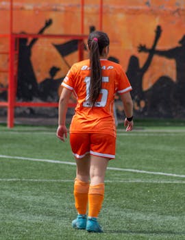 A female soccer player in orange kit during a match on a green field in Calama, Chile.