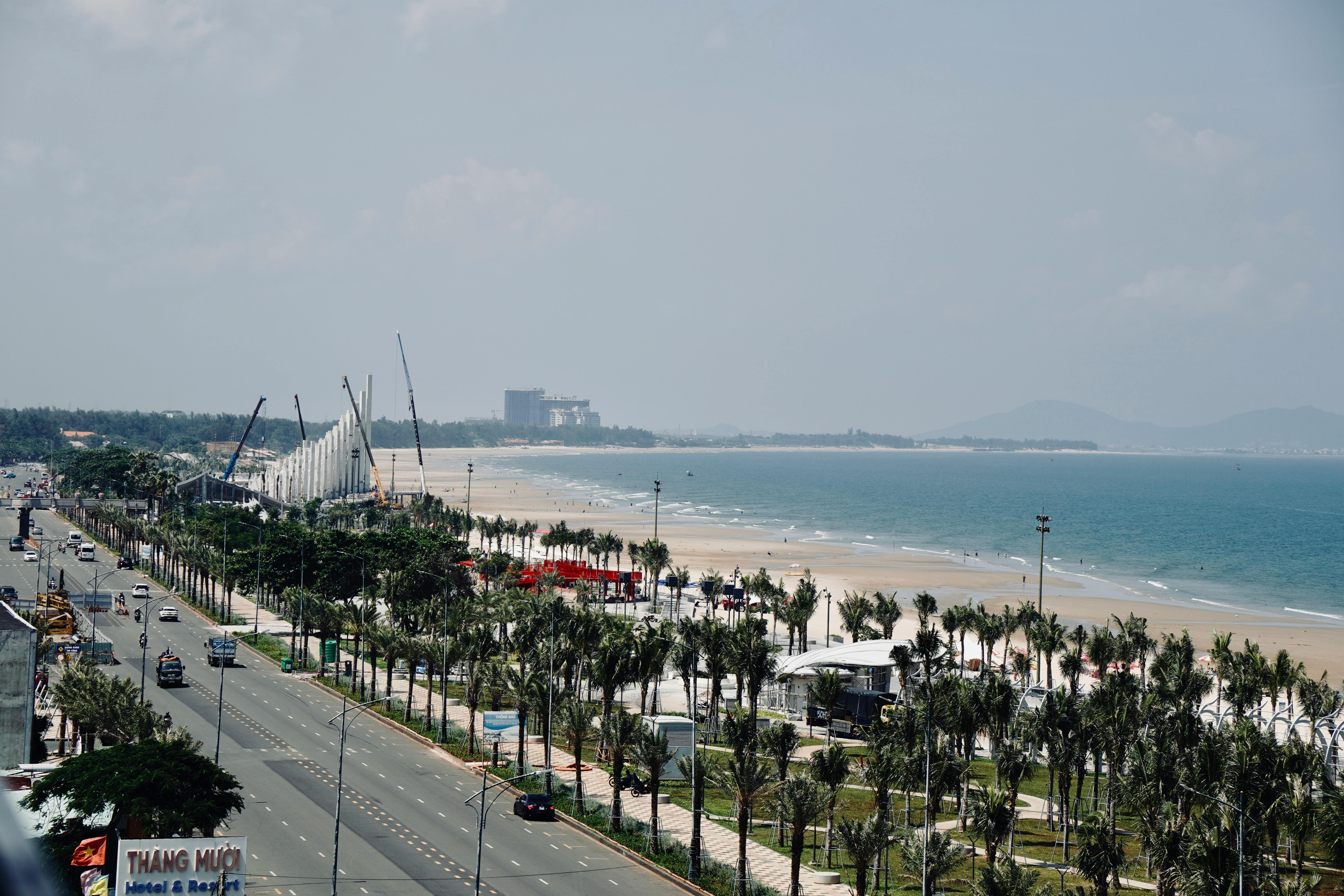 Aerial view of a coastal city with beach, highway, palm trees, and distant mountains.
