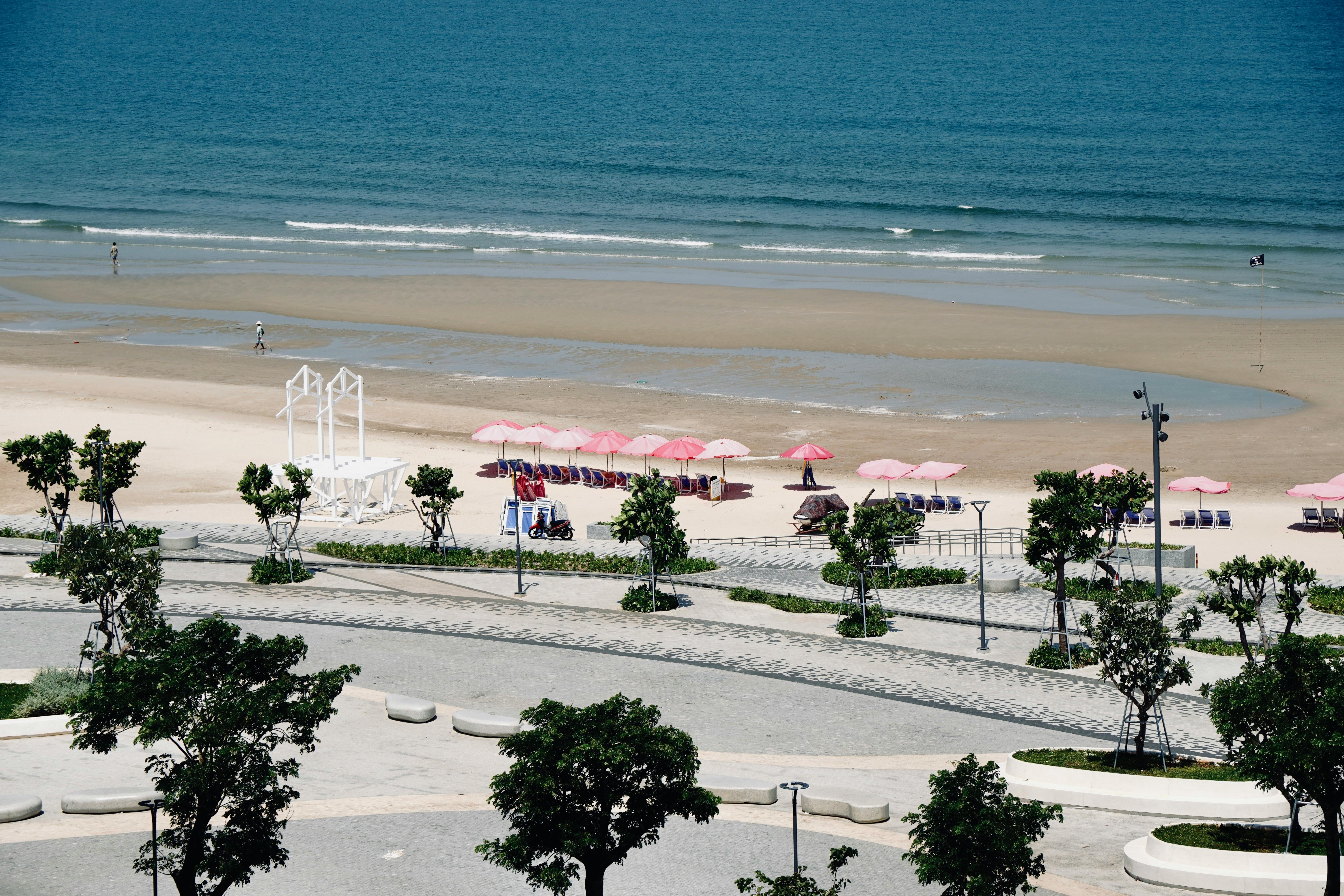 A sunny beach with pink umbrellas, clear blue ocean, and a promenade in the foreground.