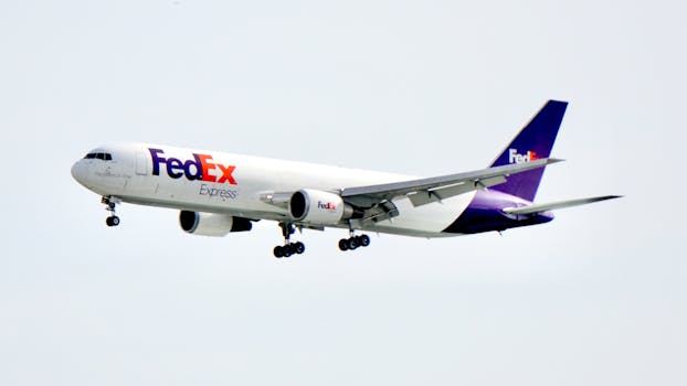 A FedEx cargo plane flying in daylight with a clear blue sky backdrop, showcasing logistics and air travel.