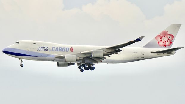 A China Airlines cargo plane flies against a cloudy sky, showcasing its iconic logo.