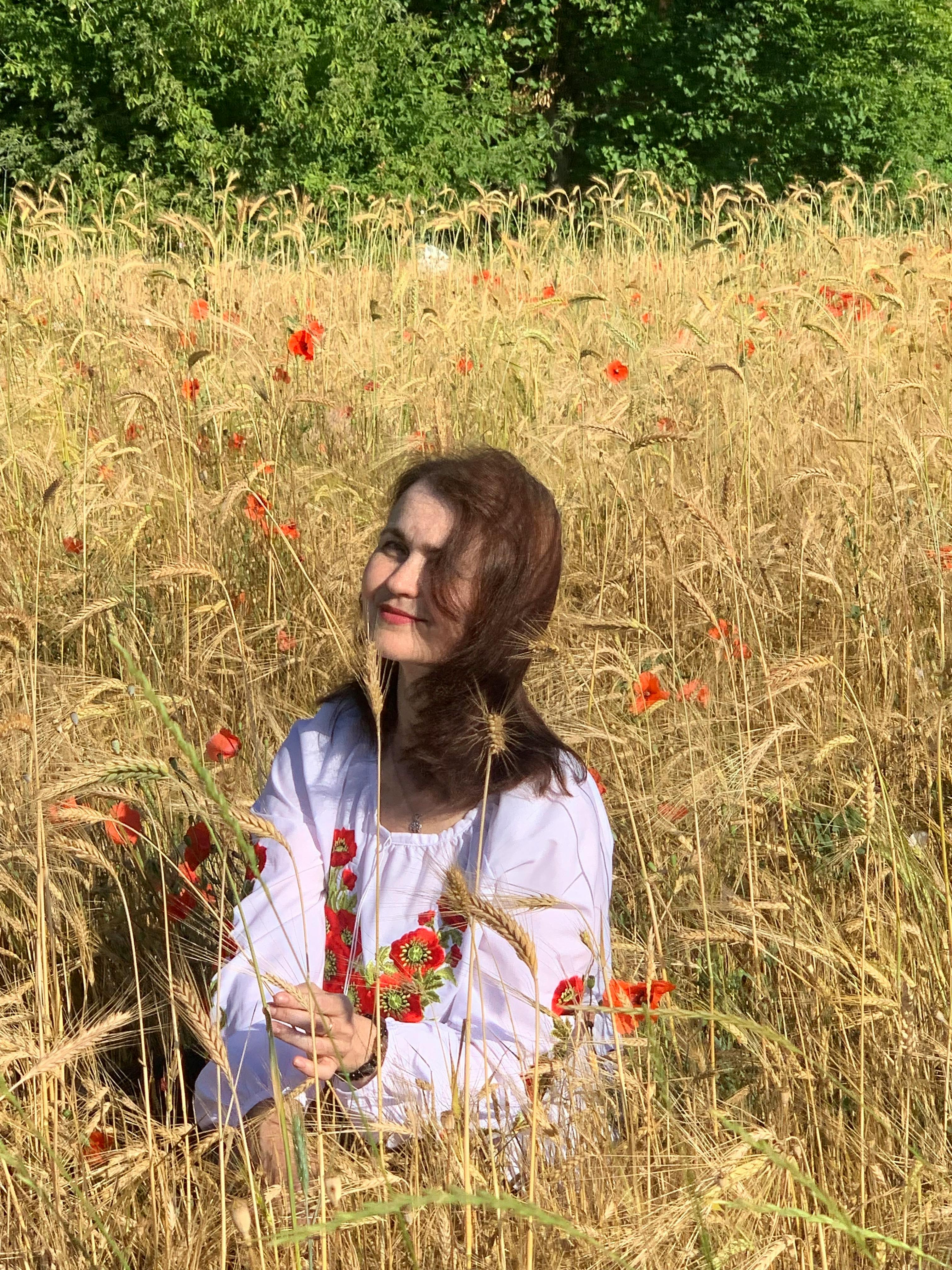 Woman in embroidered blouse sitting in sunny wheat field with poppies.