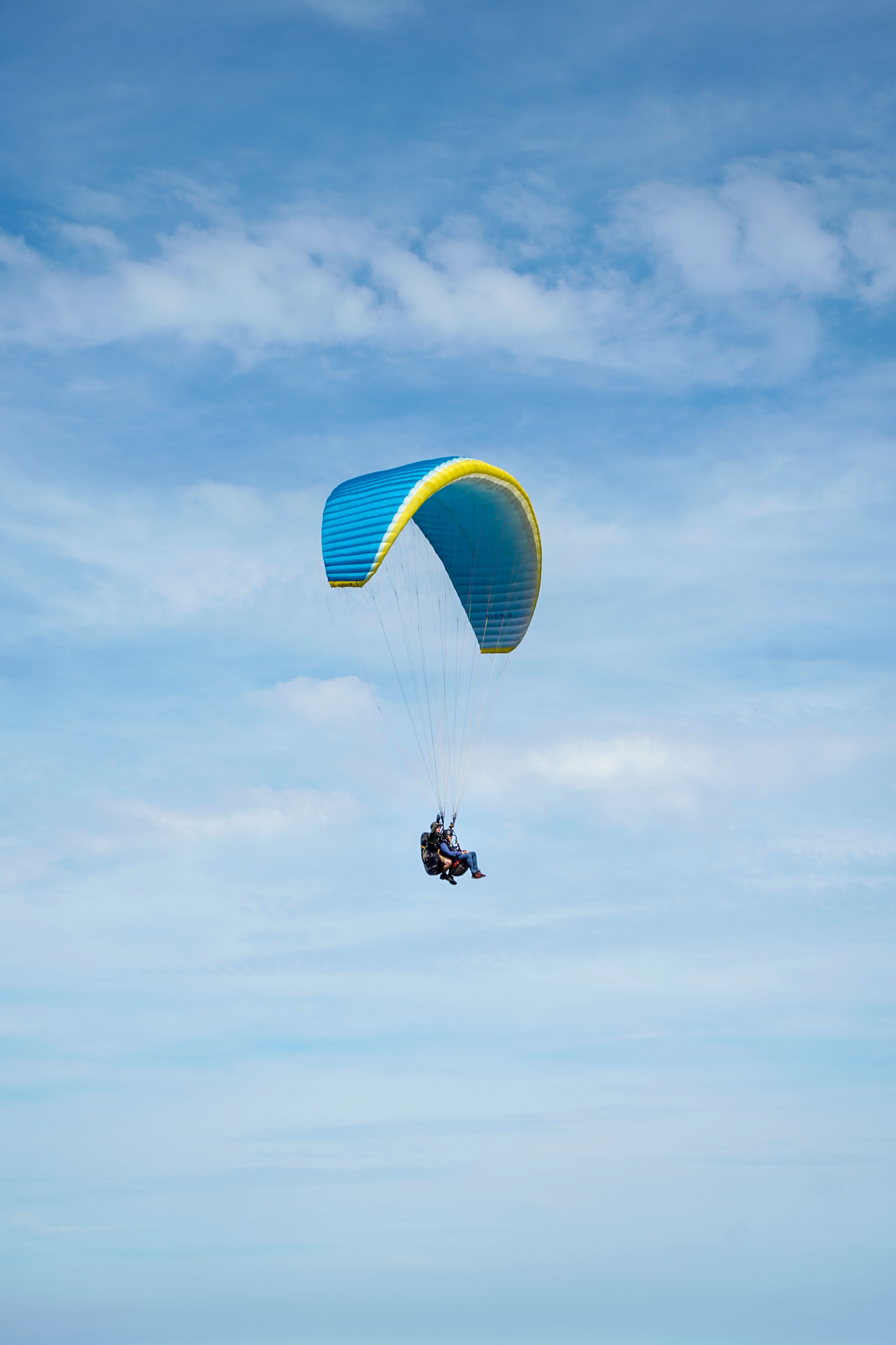 A thrilling paragliding experience with two adventurers soaring under a blue parachute in clear skies.