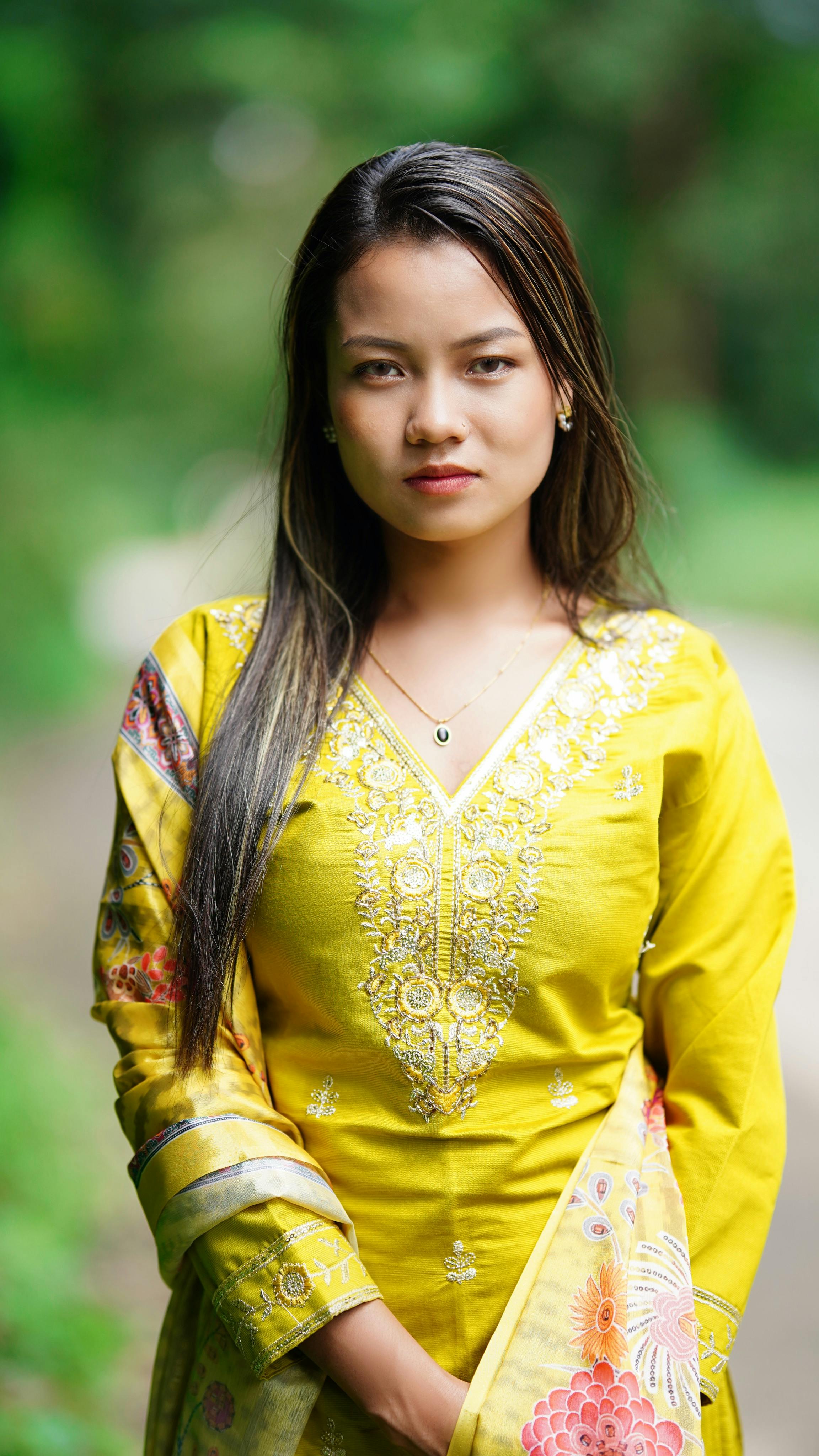 Portrait of a woman in a vibrant yellow traditional dress in a natural outdoor setting.