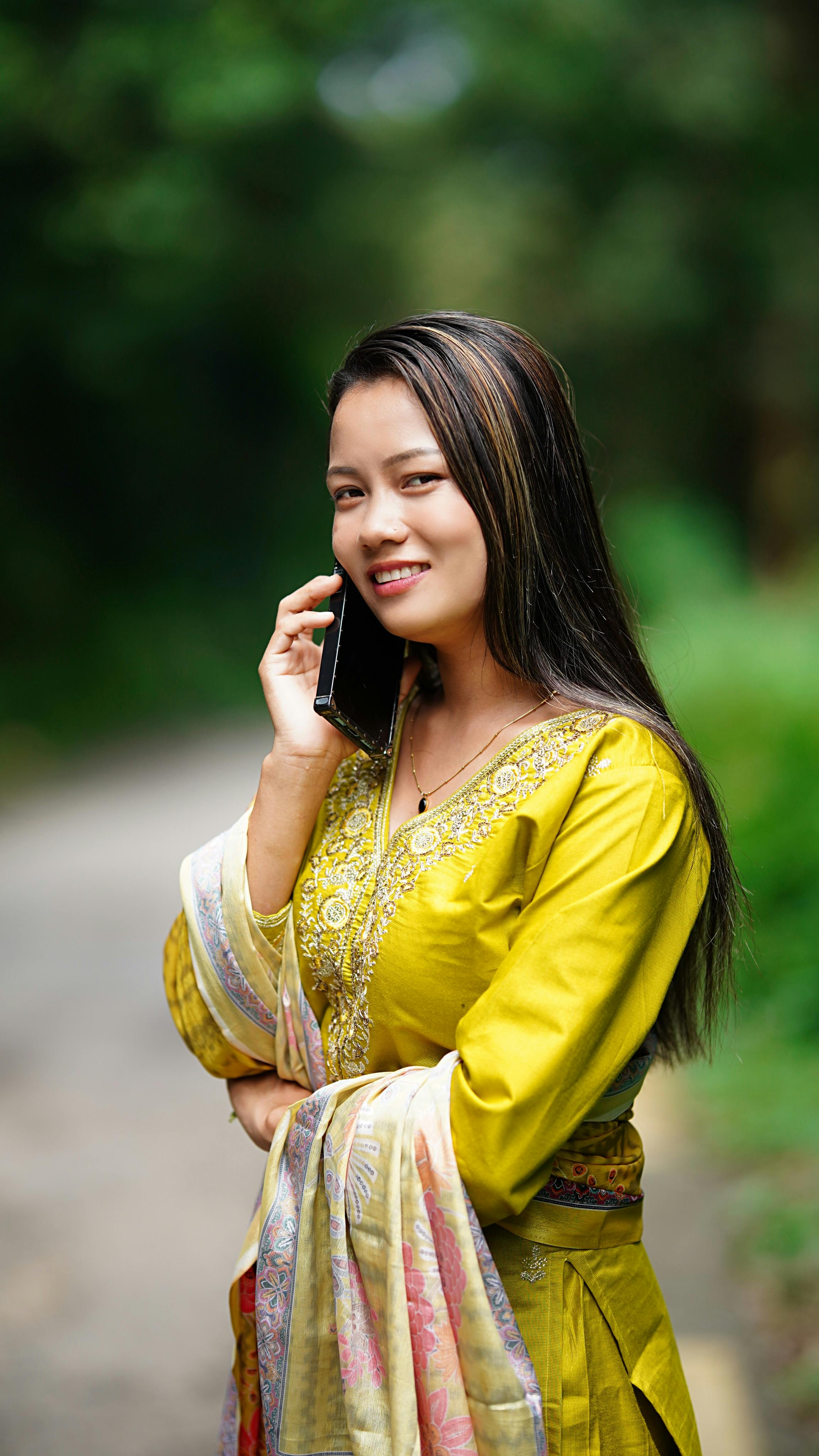 Portrait of a smiling woman in traditional attire speaking on her phone outdoors.