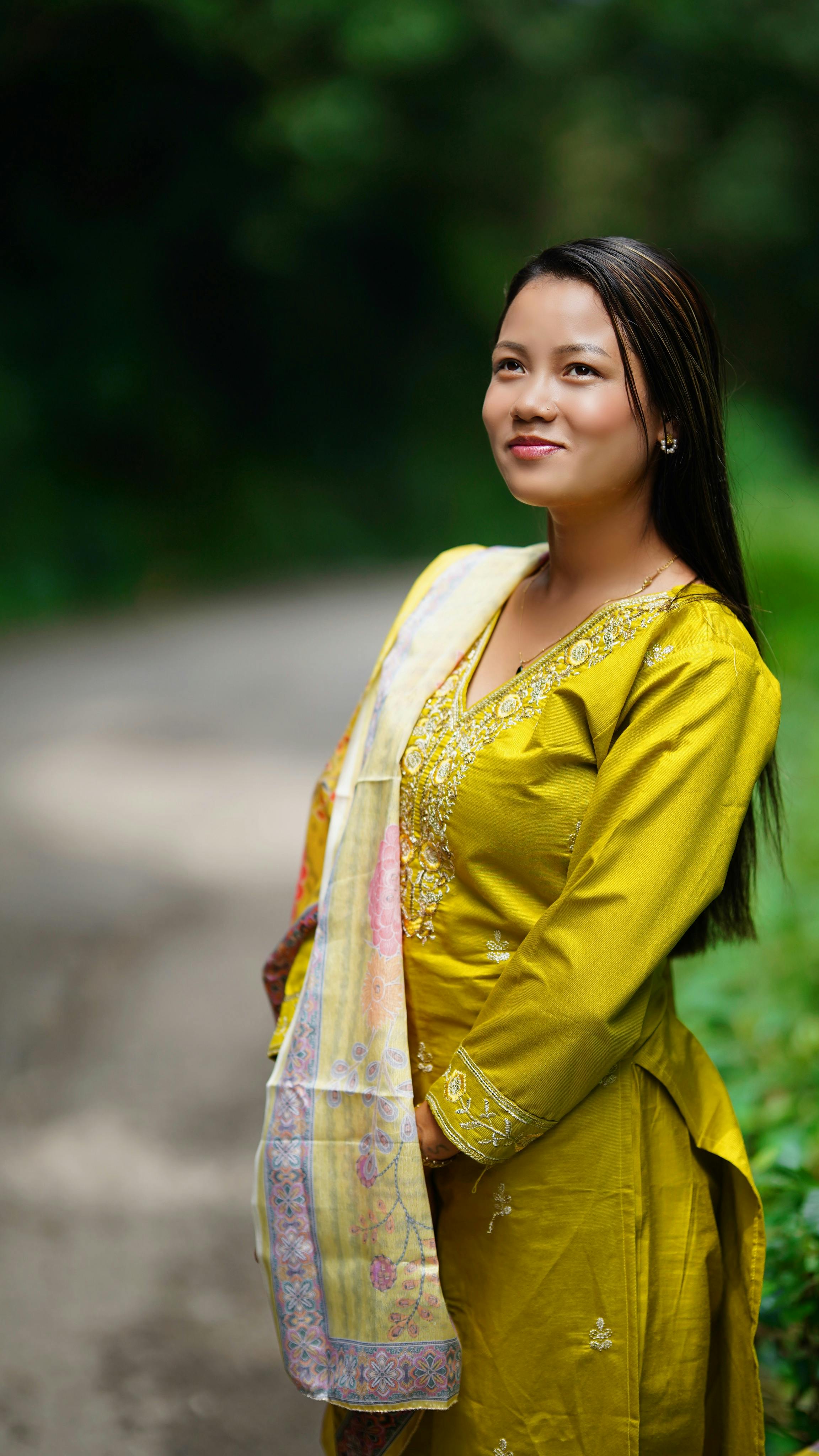 Smiling woman in vibrant yellow traditional dress standing on a rural path.
