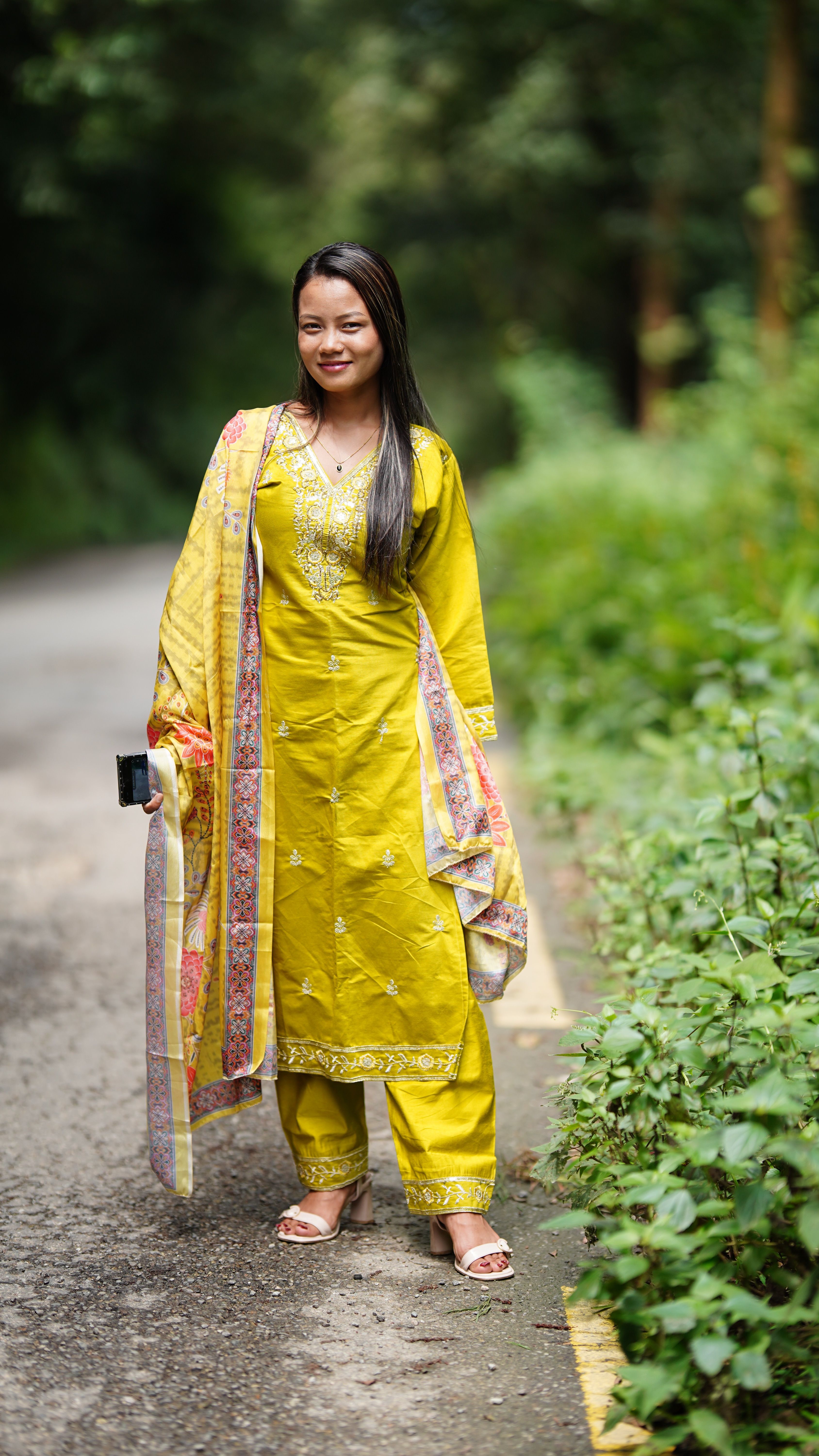 Confident woman wearing yellow traditional dress posing on a leafy pathway.