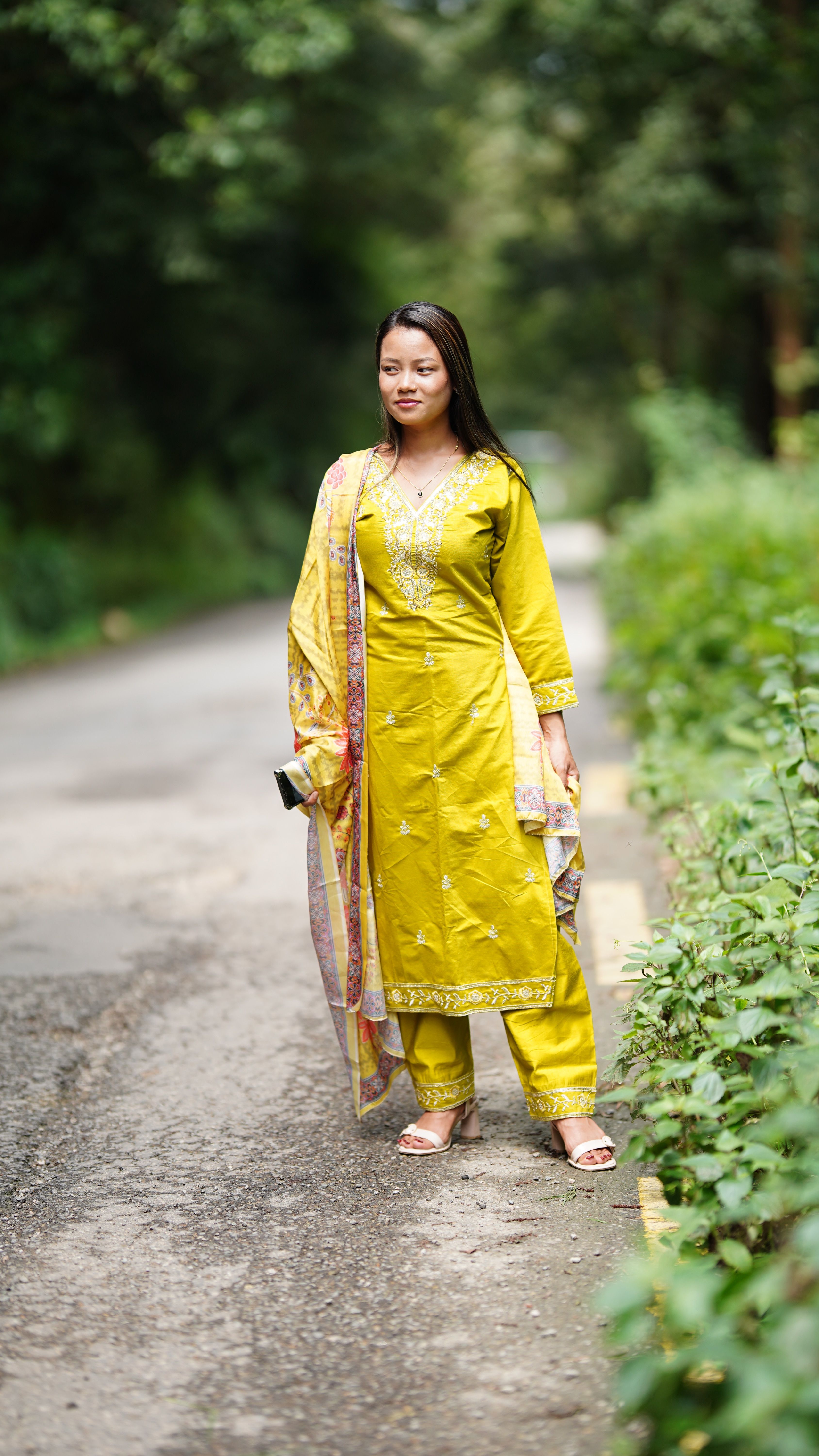 A woman in a vibrant yellow dress walking on a lush outdoor pathway.