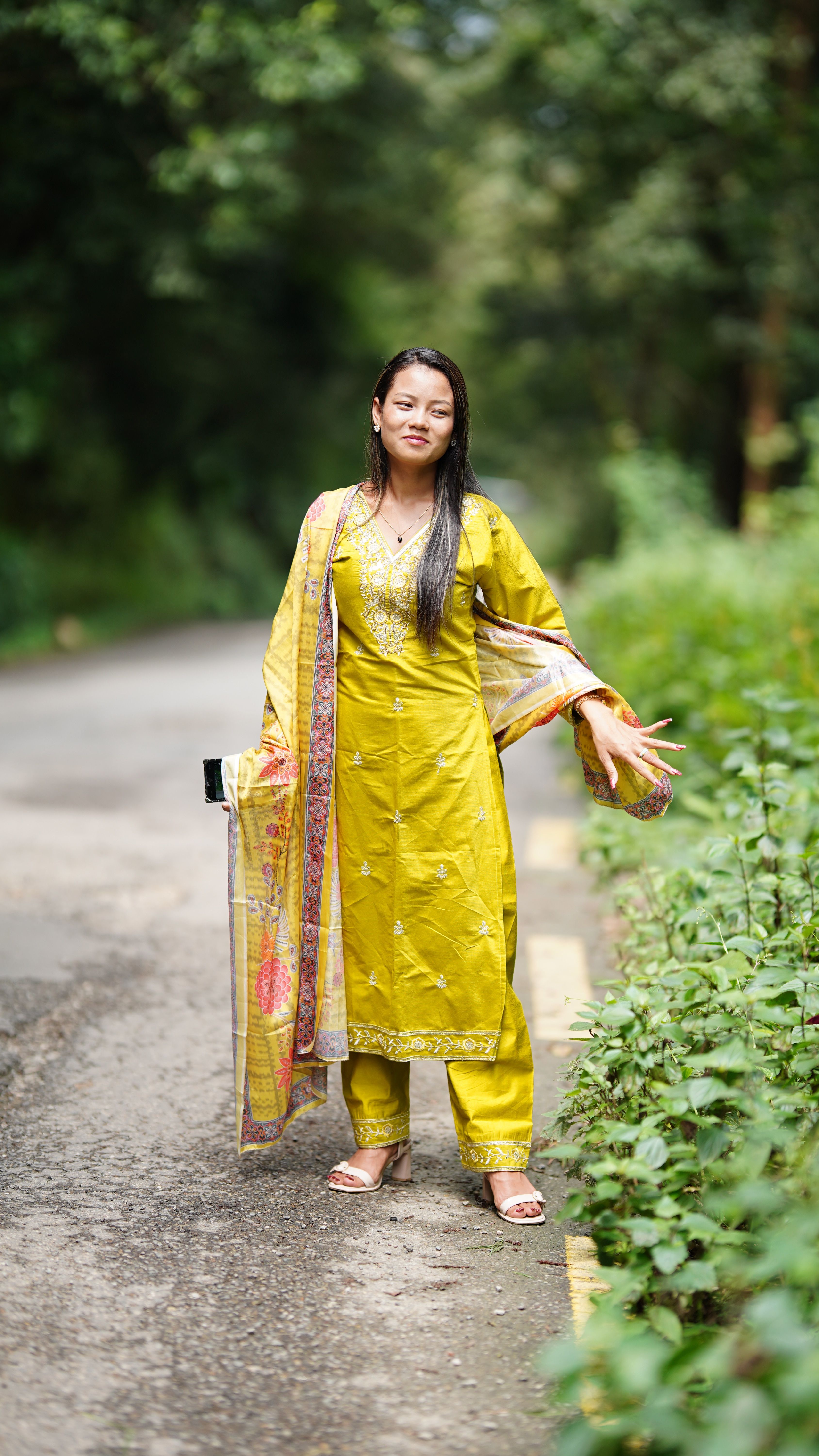 Young woman wearing vibrant ethnic attire poses on a scenic outdoor path.