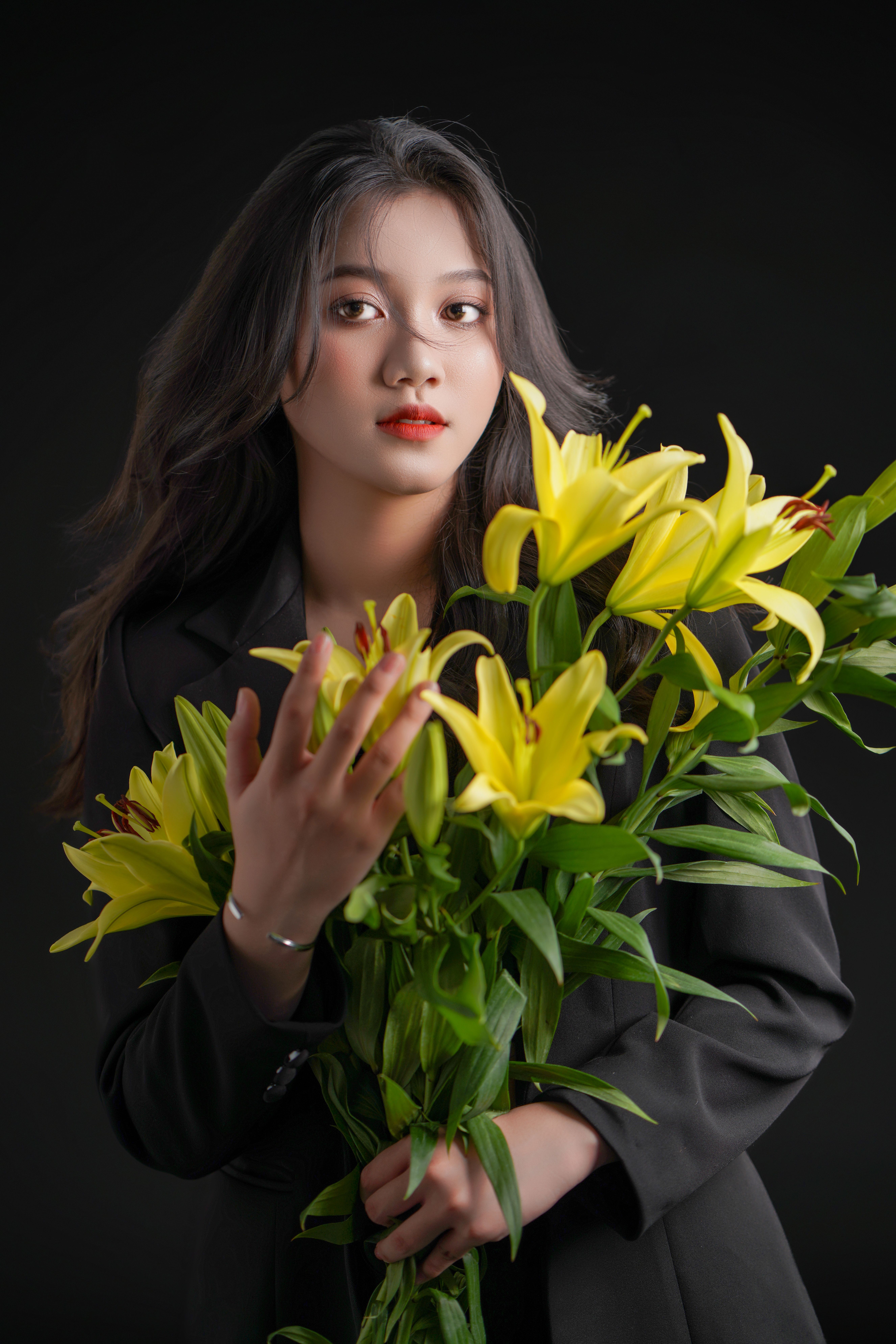 A sophisticated portrait of a woman holding a bouquet of yellow lilies, set against a dark background.