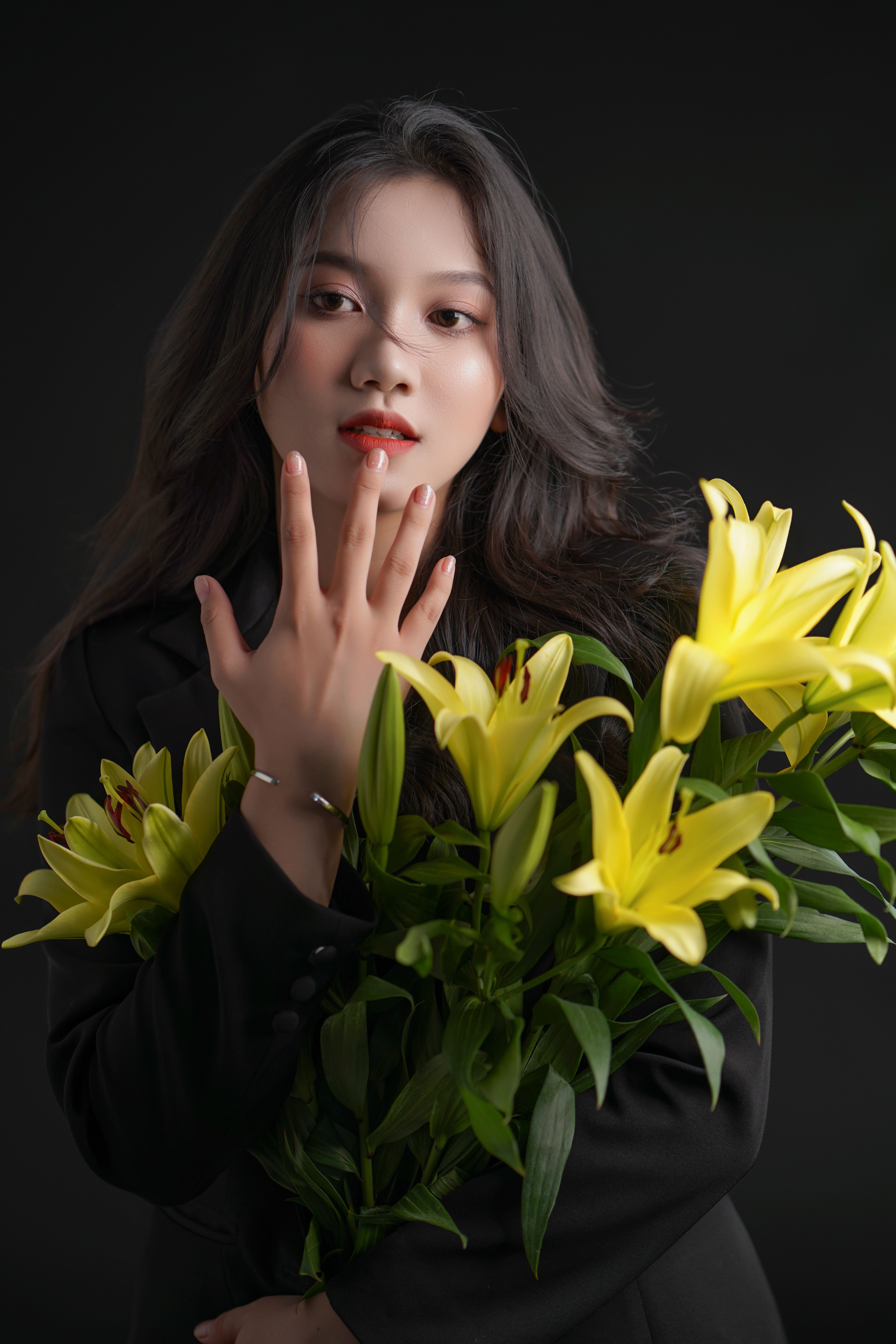 A stylish portrait of a woman in a black outfit holding vibrant yellow lilies against a dark background.