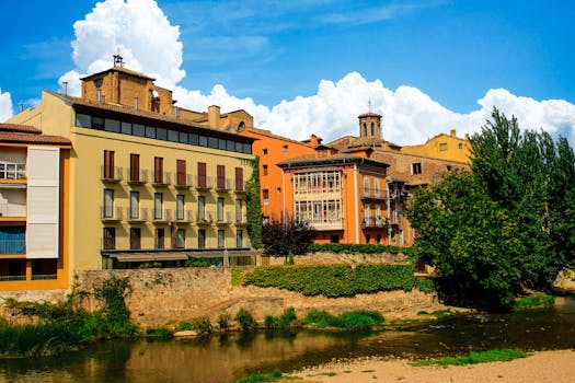 Picturesque view of historic buildings along a riverbank in Estella, Navarra, Spain with vibrant colors and a clear blue sky.