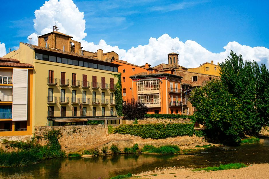 Vista pintoresca de edificios históricos a lo largo de la orilla de un río en Estella, Navarra, España, con colores vibrantes y un cielo…