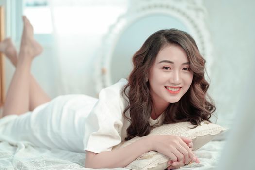 一位开朗的女子穿着白色连衣裙，躺在室内的床上放松身心，散发着舒适和幸福的气息