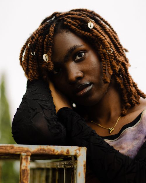 Free Artistic portrait of a woman with beaded braids leaning on a rusty rail outdoors. Stock Photo