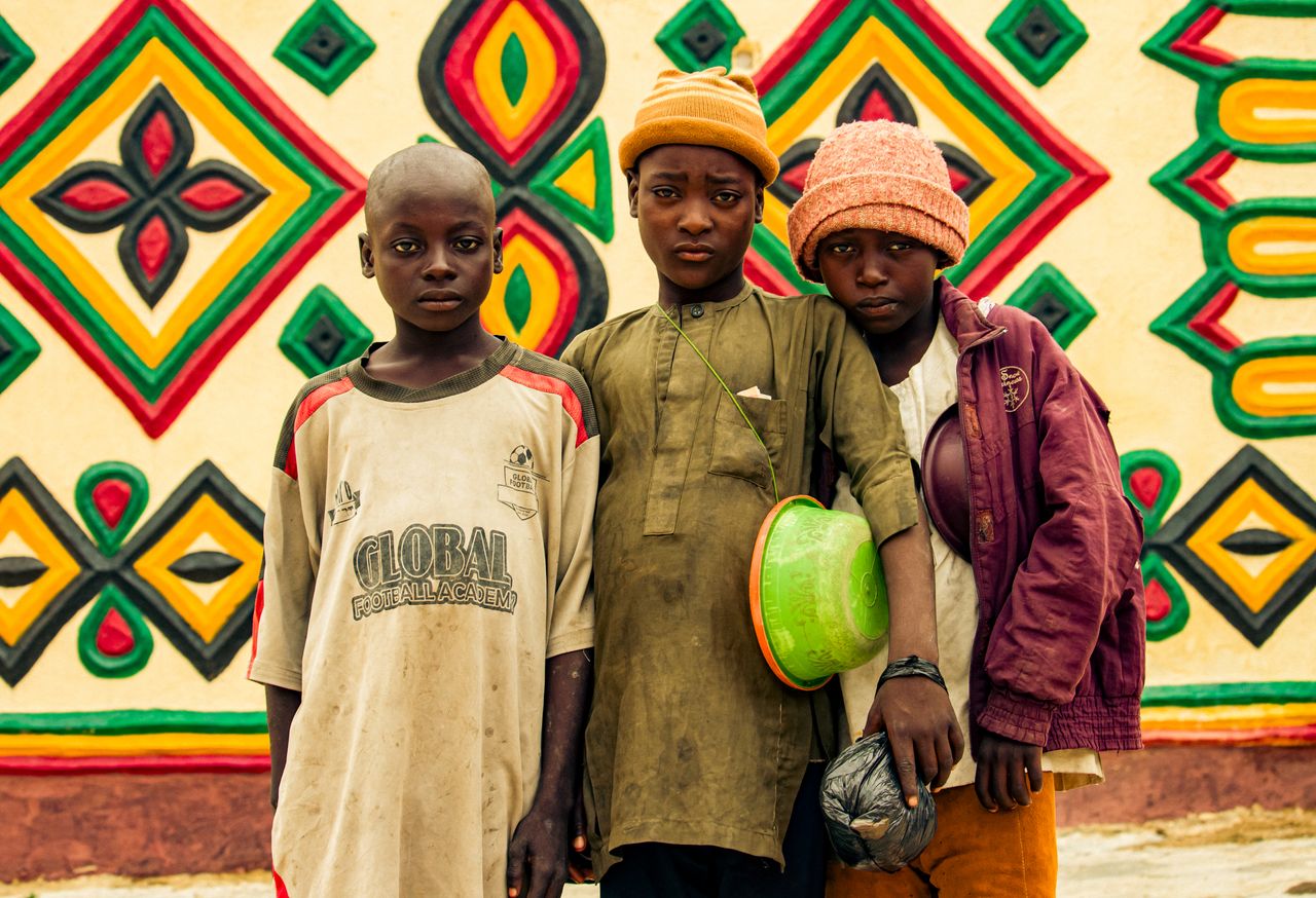 three children stand in front of a colorful geometric mural showcasing
